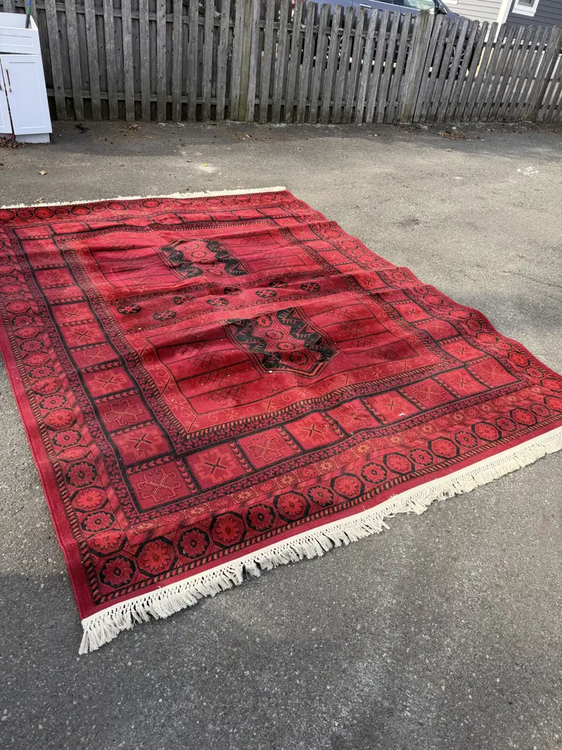 A red rug with white fringe laid out on pavement
